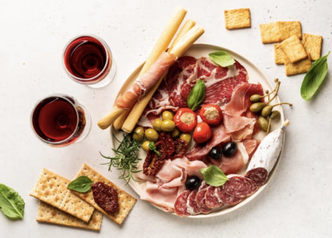 assiette de charcuterie avec des olives et des gressins. Il y a également deux verres de vin rouge pour bien mettre en valeur le vin de Bourgogne idéal pour une belle soirée d'été.  