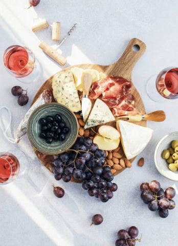 planche apéritive en bois avec du raisin noir, de la charcuterie, du fromage, des olives et des verres de vin rosé. 
met bien en avant le vin de bourgogne pour une soirée d'été